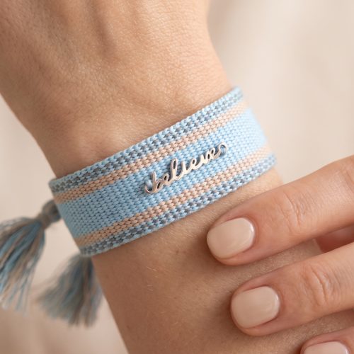 Geweven armband met believe-bedel gedragen om de pols