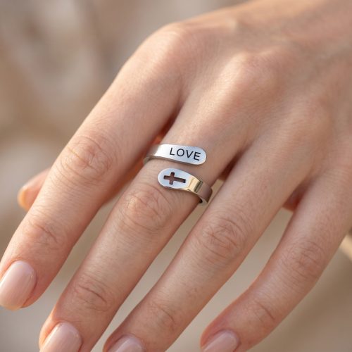 Zilveren ring met kruisje en het woord Love gedragen aan de hand